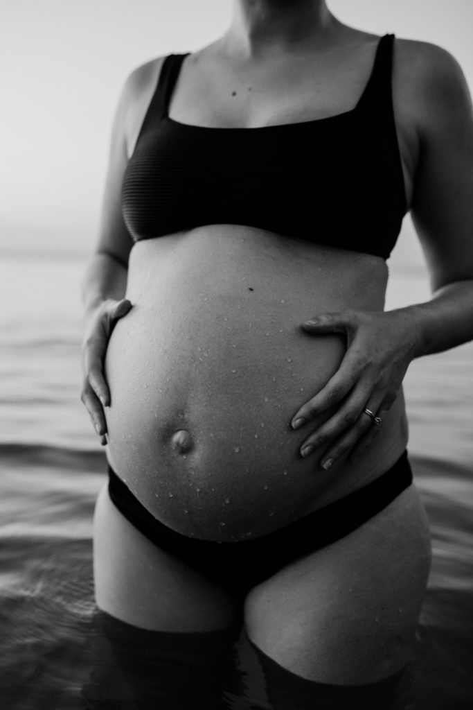 black and white image of water drops on pregnant belly during beach maternity photos, And So I Don't Forget Photography