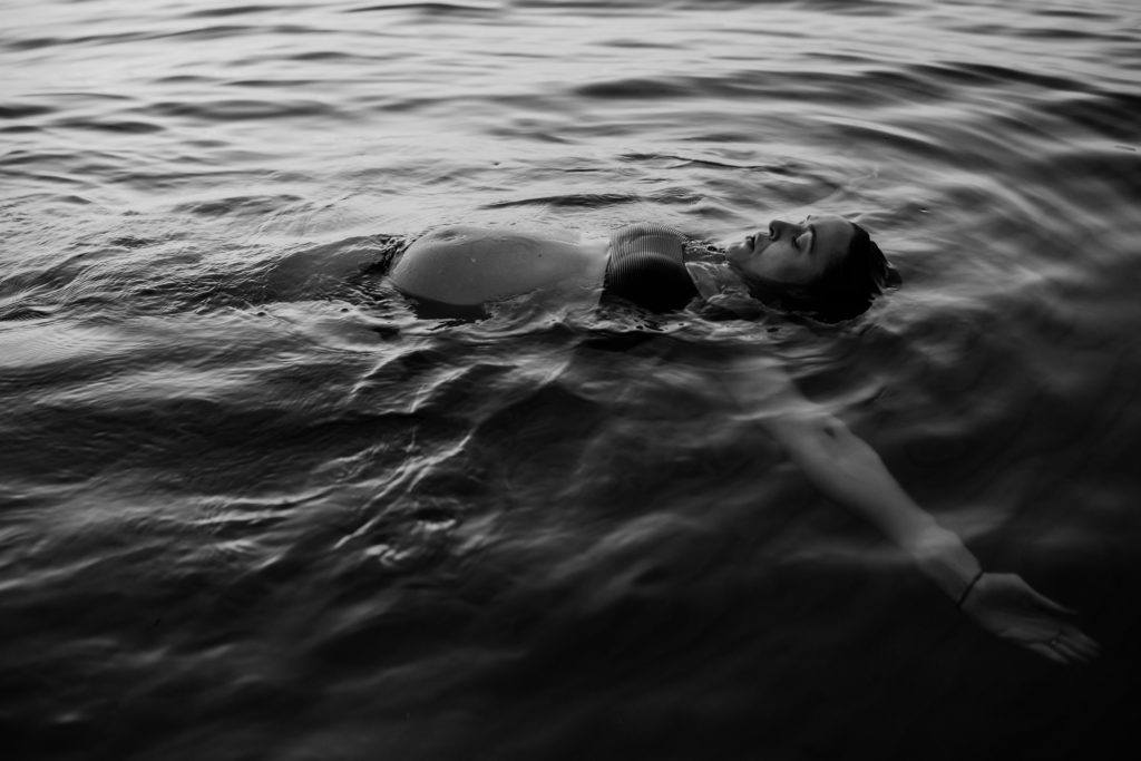 black and white photo of pregnant woman floating in ocean for beach maternity photos, And So I Don't Forget Photography