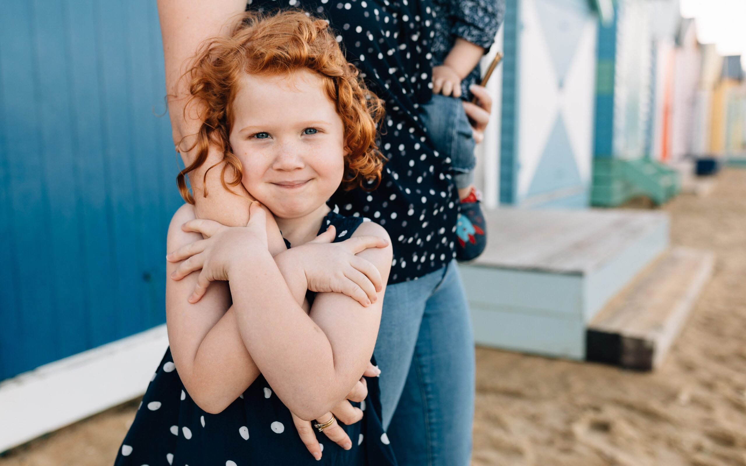Girl hugging Mum's hand during family photography session at Brighton Beach Bathing Boxes