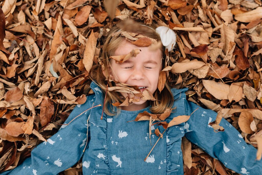 girl lying in autumn leaves with eyes closed by Delanie, Melbourne family photographer, during outdoor family photography session with autumn leaves