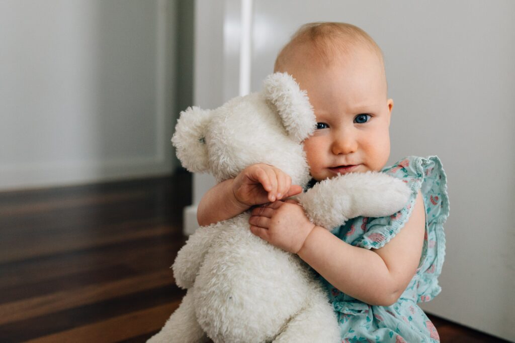 1 year old girl hugging teddy bear while staring at camera