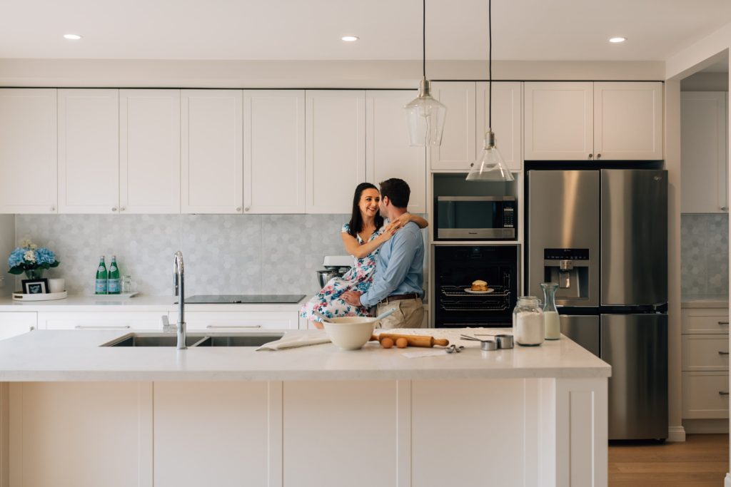 bun in the oven pregnancy announcement with couple hugging in kitchen by Melbourne photographer