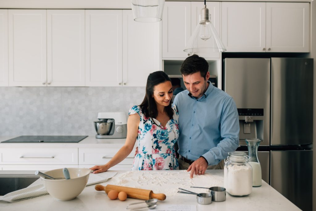 man and woman standing at bench with baking ingredients for funny bun in the oven pregnancy announcement photography session
