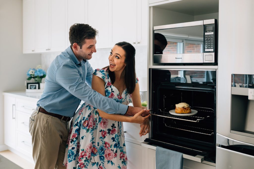 man and woman smiling at each other with bun in the oven pregnancy announcement photography session