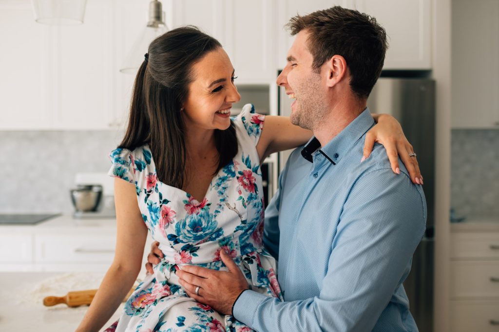 man and woman laughing in kitchen during bun in the oven pregnancy announcement photography session by Melbourne photographer