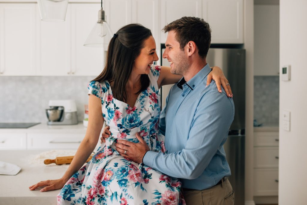 husband and wife laughing together, bun in the oven pregnancy announcement photography session