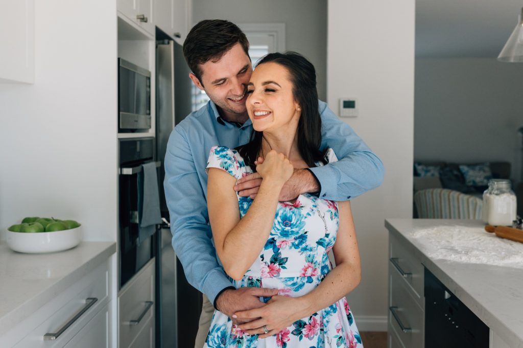 man's arms around woman wearing floral dress, bun in the oven pregnancy announcement photo session