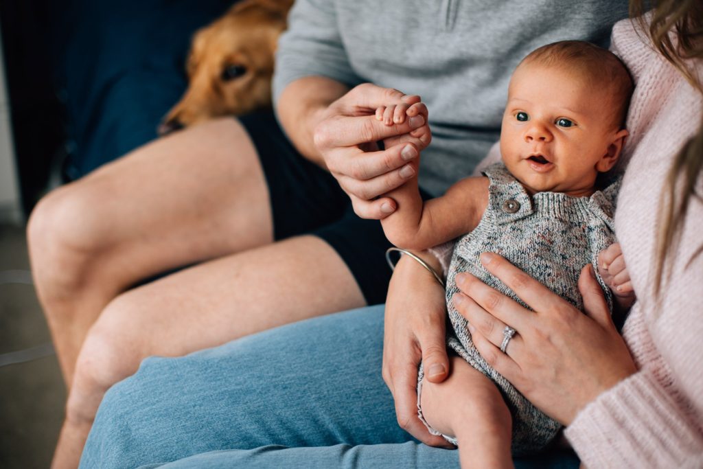 Newborn baby holding Dad's hand while in Mum's arms, showing example of newborn photoshoot outfit