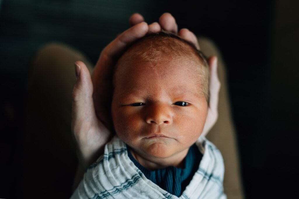 Baby looking up at camera, head cradled in dad's hands, Fresh 48 at St Vincent's Private