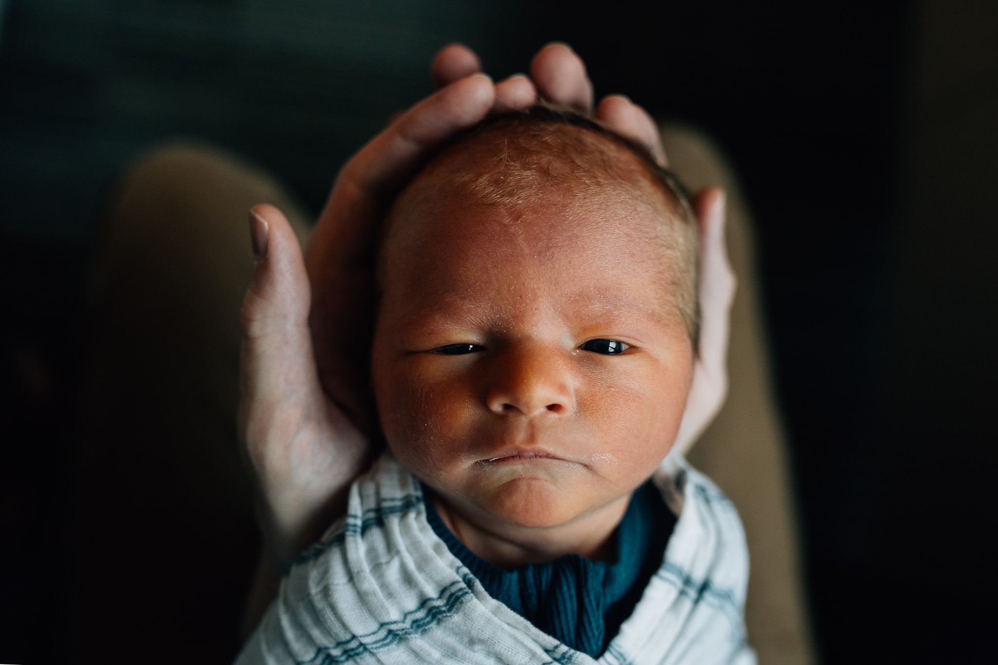 Baby looking up at camera, head cradled in dad's hands.