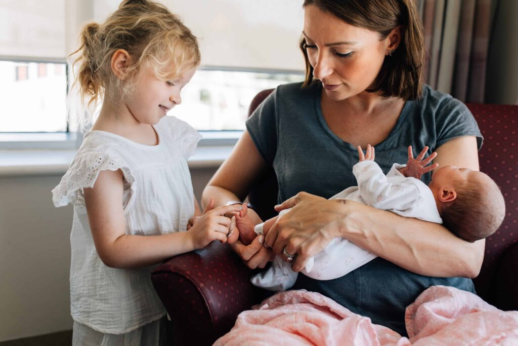 Girl touching baby's foot as she meets newborn sibling