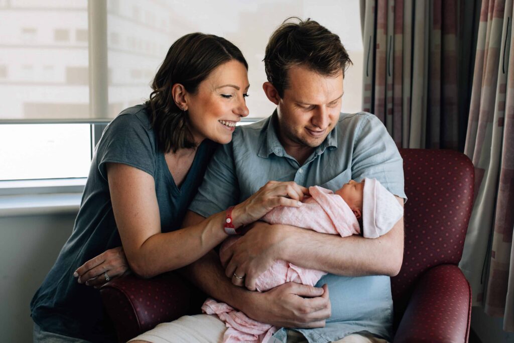 Mum and dad smiling and ooking down at newborn baby